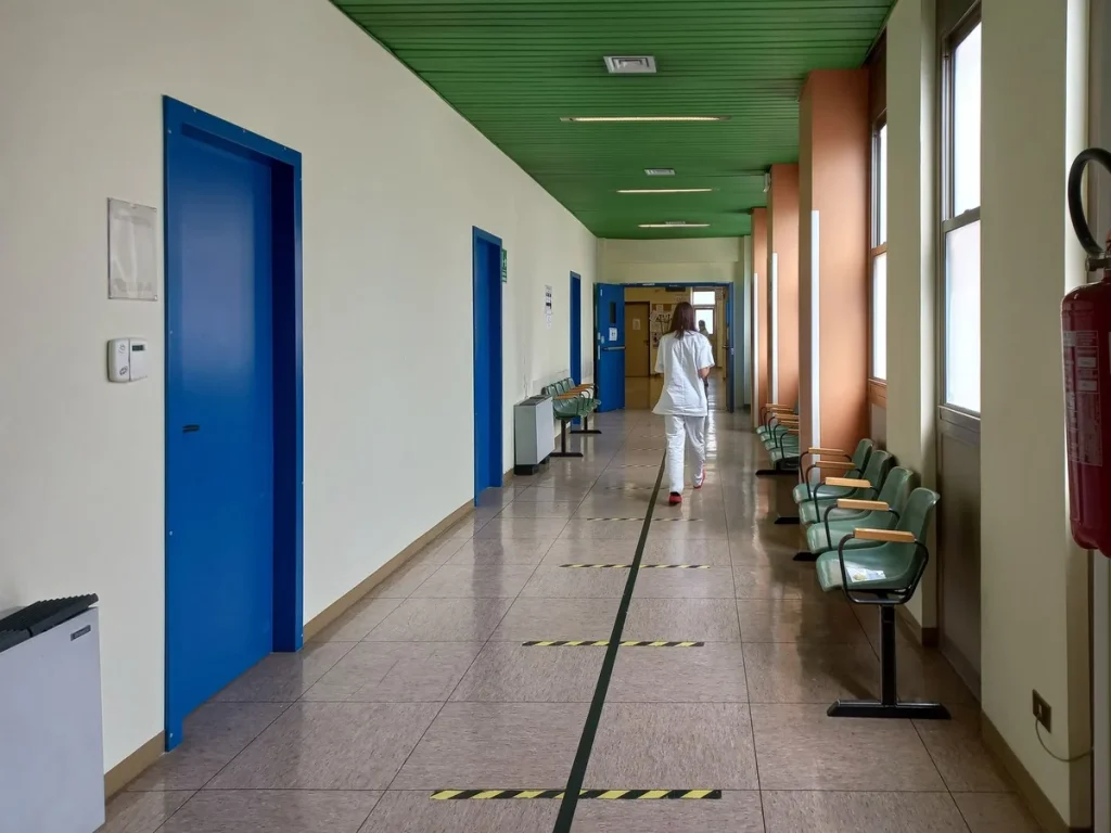 Une personne assise seule dans une salle d'attente médicale, vue de dos, dans un environnement clinique.