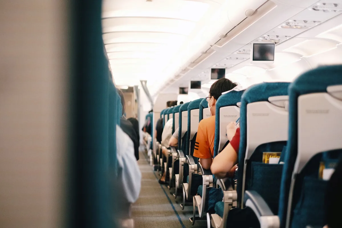 Personne appliquant une crème hydratante sur son visage dans un siège d'avion avec des produits de beauté sur la tablett