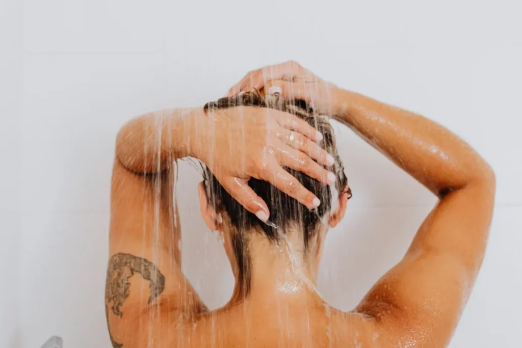 Mains tenant un gel douche crémeux sous l'eau chaude avec vapeur et lumière naturelle