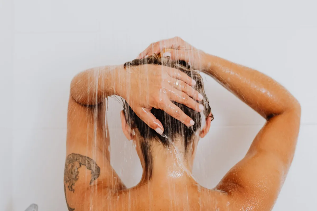 Mains tenant un gel douche crémeux sous l'eau chaude avec vapeur et lumière naturelle