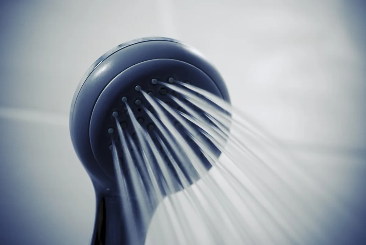 Personne préparant la peau sous une douche tiède, serviette et gel doux à portée de main