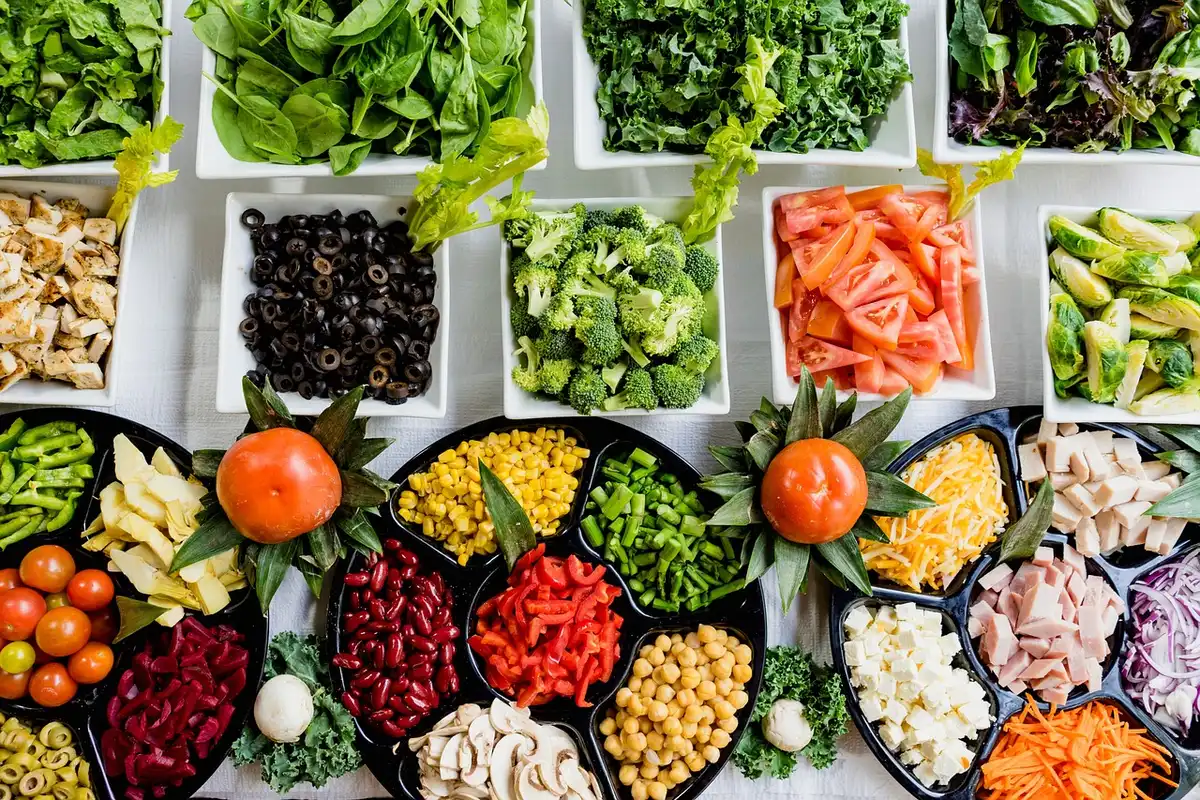 Personne anonyme notant un journal alimentaire à une table ensoleillée avec salade et calculatrice